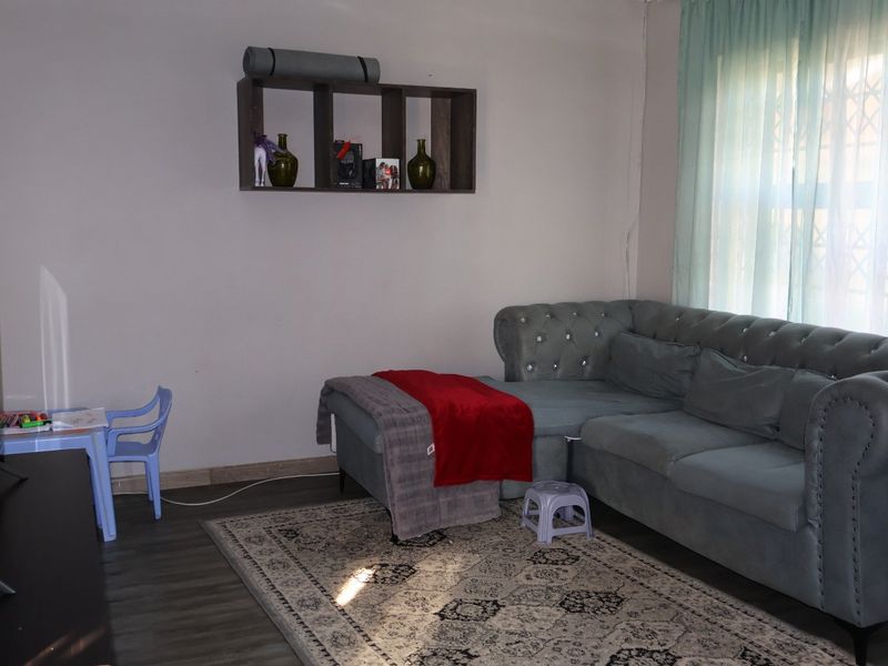 A living room featuring laminate flooring, a wall-mounted shelving unit, and a window fitted with a security gate.