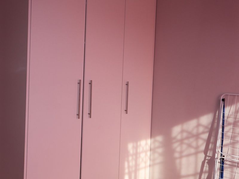 A bedroom interior featuring a built-in wardrobe with modern metal handles, illuminated by natural light casting window shadows on the wall.