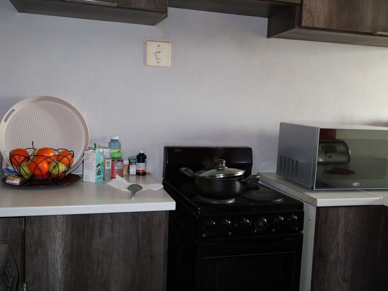 A functional kitchen area featuring dark wood-look cabinetry, laminate countertops, and a freestanding electric stove with an integrated microwave.