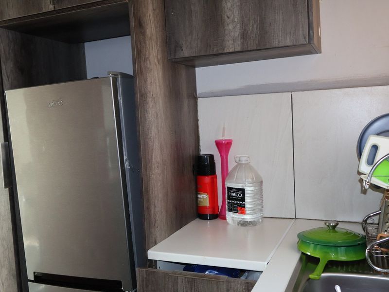 A compact kitchen area featuring wood-look built-in cabinetry, a laminate countertop, and a dedicated housing unit for a refrigerator.