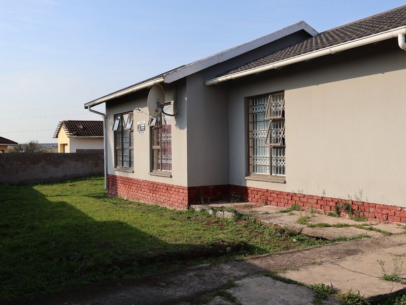 Rear view of the house featuring a brick plinth, security bars on windows, and a concrete paved area requiring maintenance.