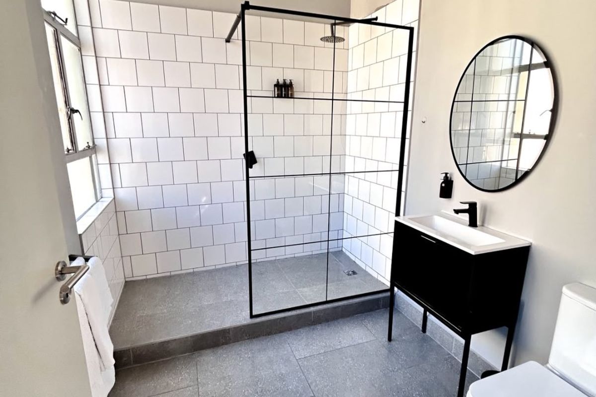 Modern bathroom featuring a walk-in shower with black-framed glass screen, subway tiling, contemporary vanity, and sleek grey floor tiles.