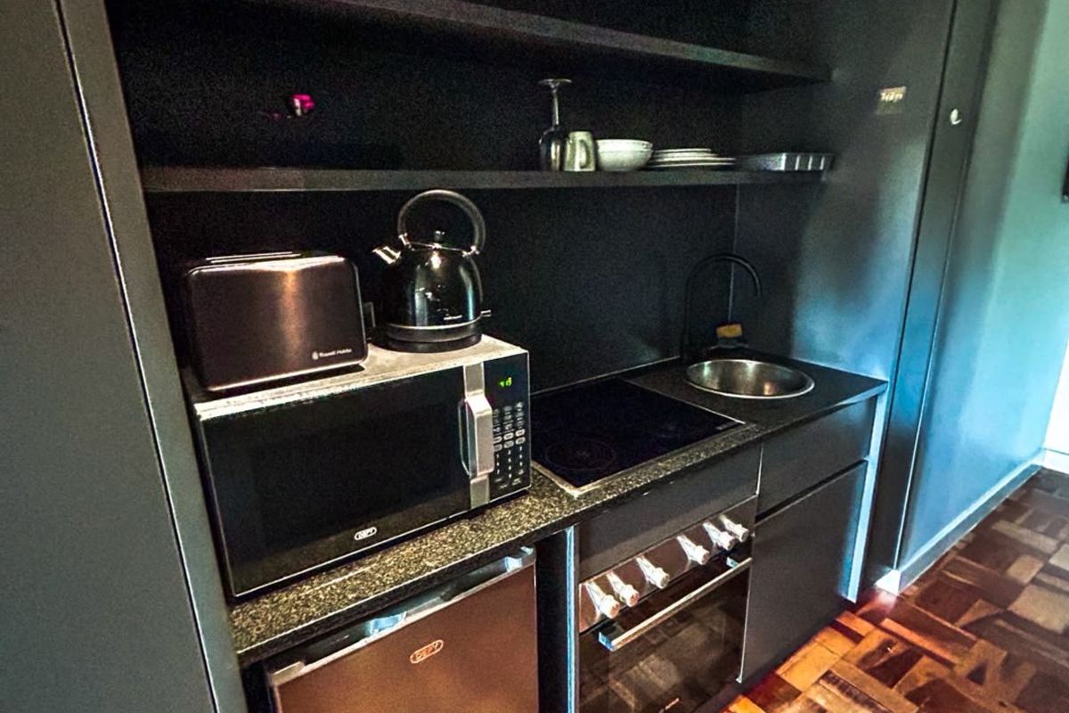 Compact modern kitchen featuring dark cabinetry, granite countertops, built-in oven, electric hob, and stylish parquet flooring.