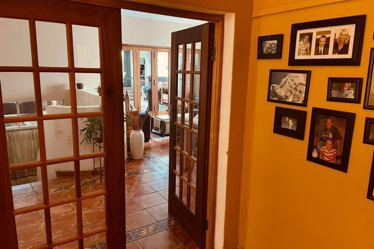 A hallway featuring terracotta floor tiles and timber-framed French doors leading into an adjacent living space.