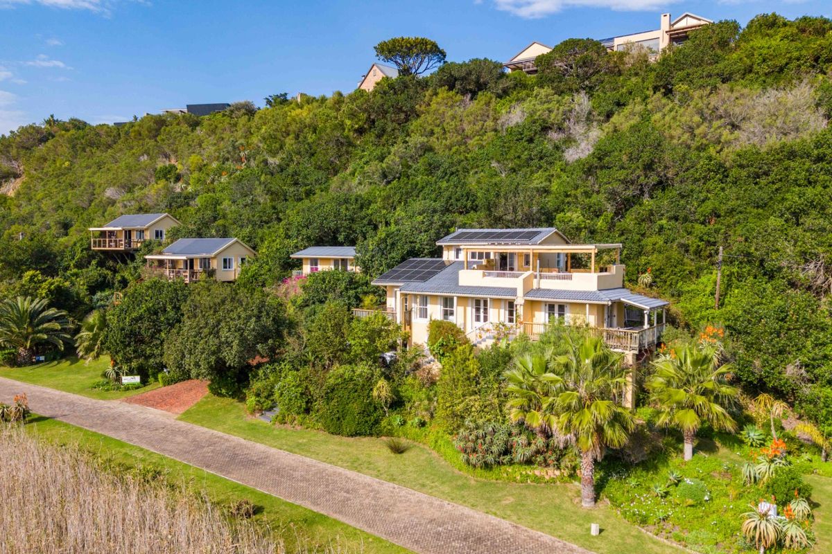 Aerial view of a multi-level residential property nestled in a lush, hillside landscape, featuring solar panels, timber decking, and a paved driveway.