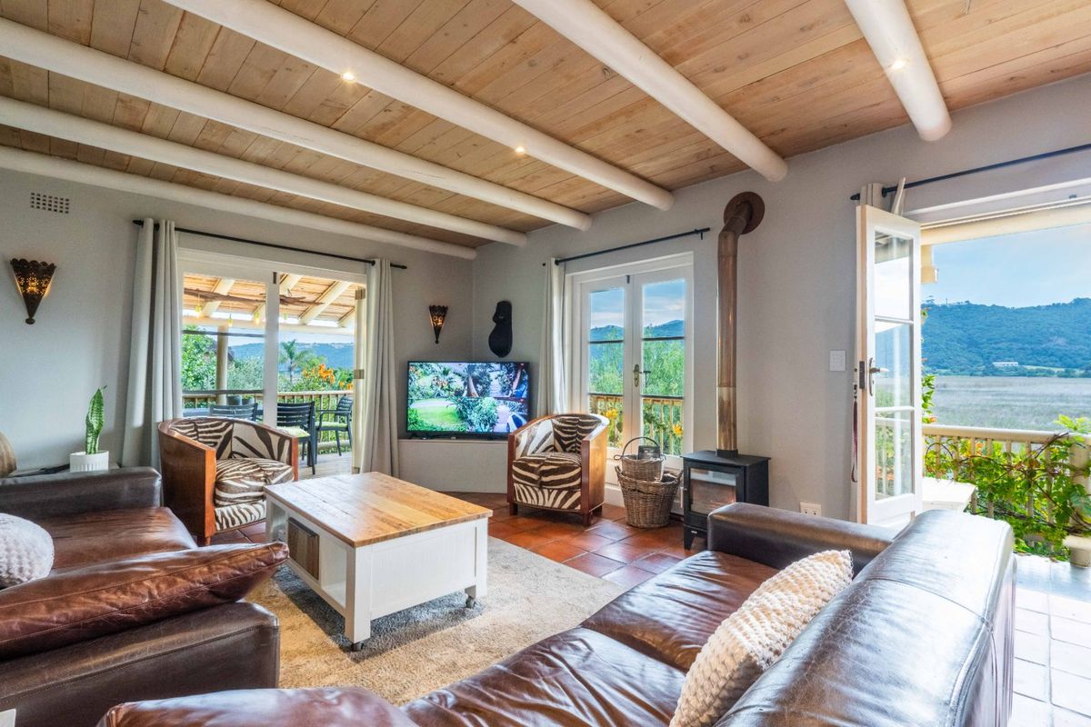 Spacious living room featuring exposed timber beam ceilings, terracotta flooring, and a freestanding wood-burning fireplace, with direct access to a scenic outdoor patio.