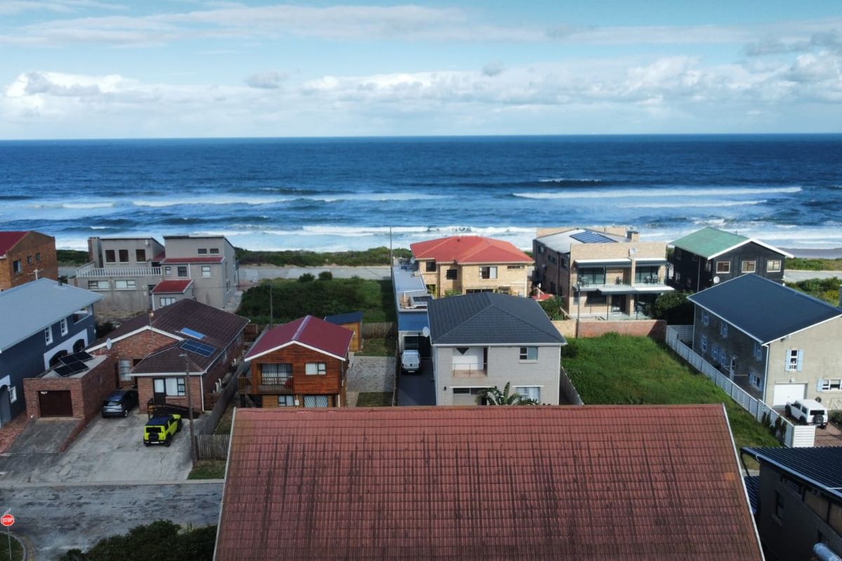 An aerial view of a coastal residential neighborhood featuring various homes with tiled roofs, situated directly along the oceanfront.