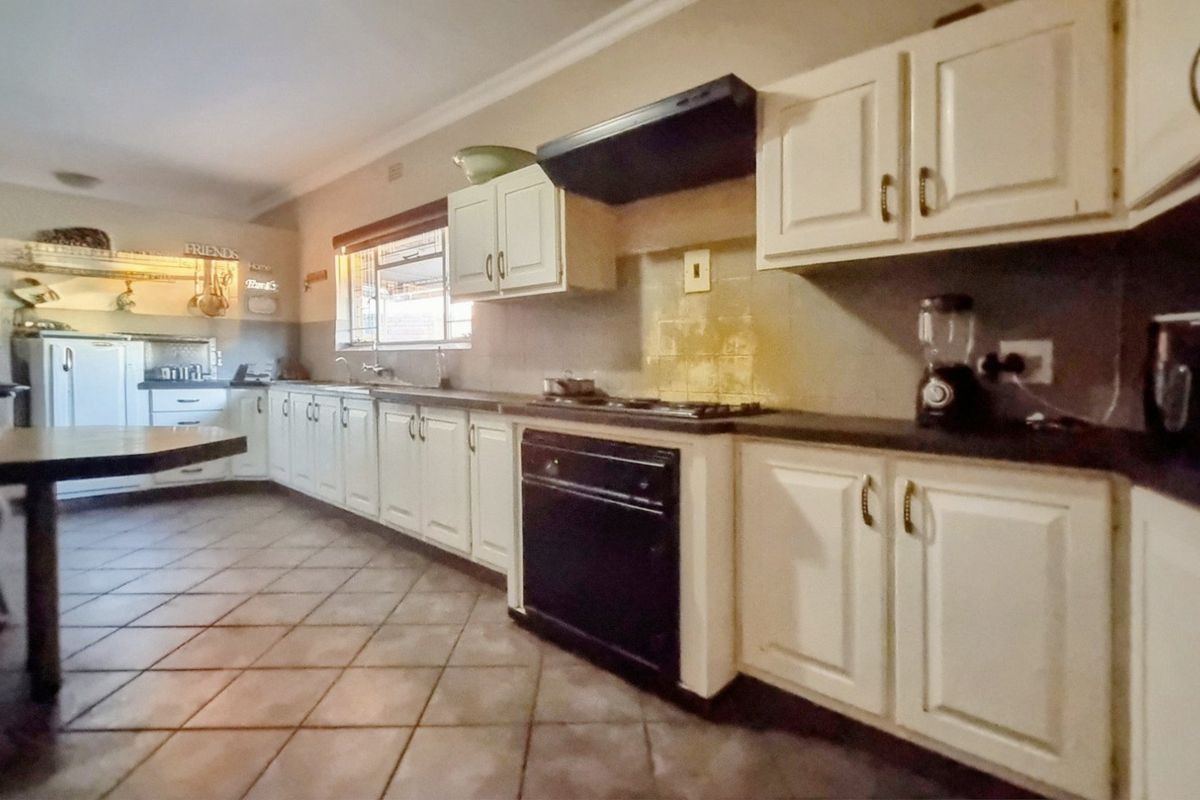A functional kitchen featuring white cabinetry, built-in oven, gas hob, extractor fan, and tiled flooring with a spacious layout.