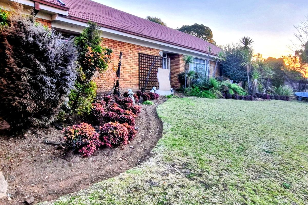 A view of the rear brick facade of the house featuring a well-maintained garden with established shrubs and a tiled roof.