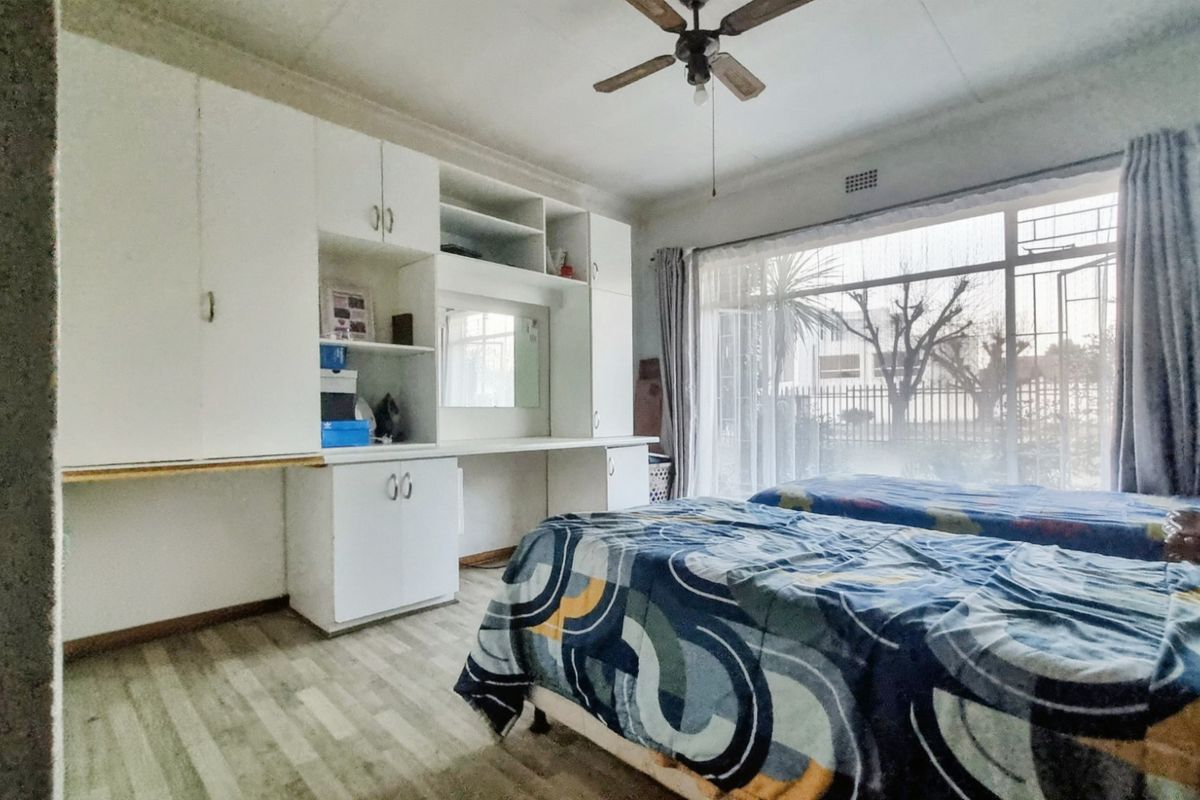 A bedroom featuring built-in white cabinetry, a ceiling fan, and large windows with security bars, offering a functional and well-lit living space.