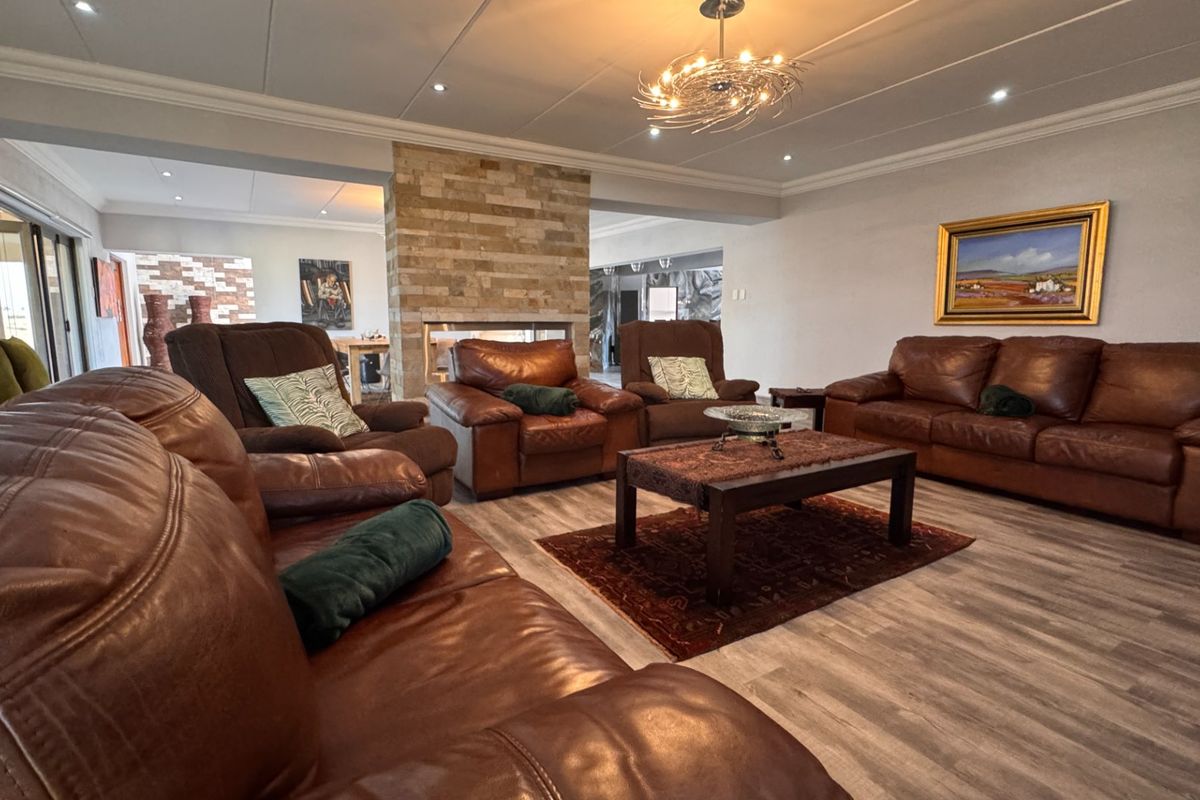 Spacious living room featuring a central stone-clad fireplace, recessed downlighting, and modern laminate flooring, creating a warm and inviting atmosphere.