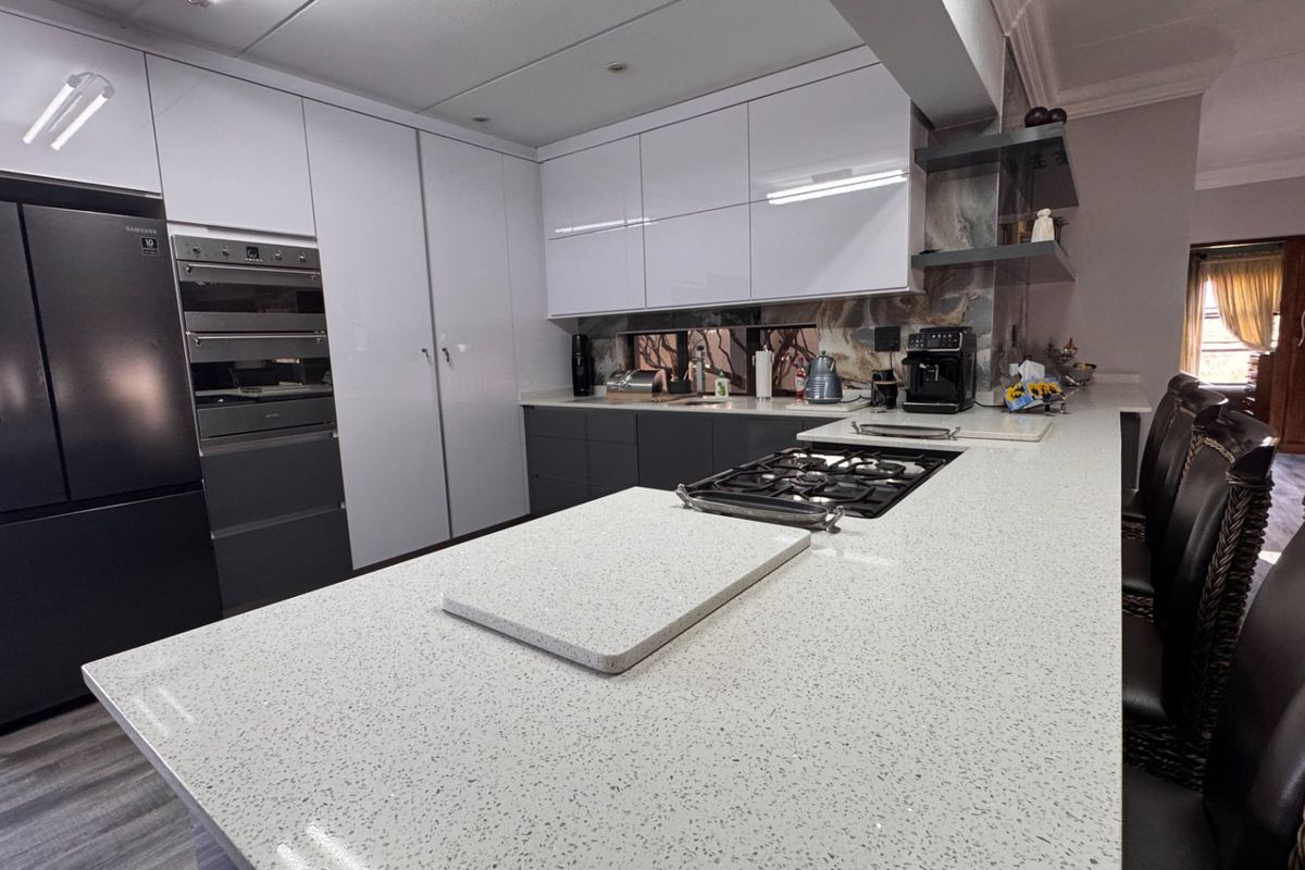 Modern kitchen featuring sleek white and grey cabinetry, quartz countertops, a central island with a gas hob, and high-end built-in appliances.