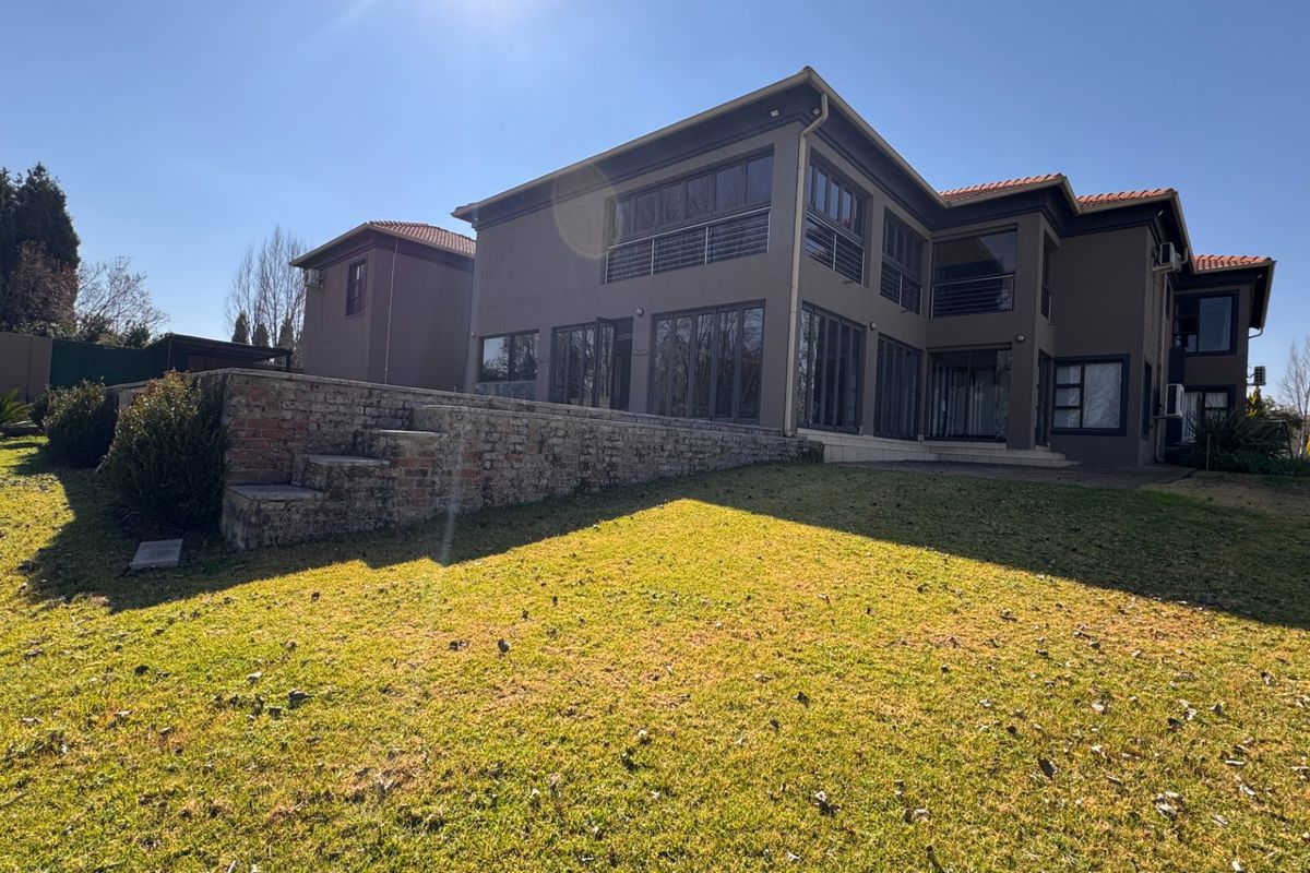 Rear view of a multi-story residential property featuring a large lawn, brick retaining wall, and extensive glass sliding doors leading to a balcony.