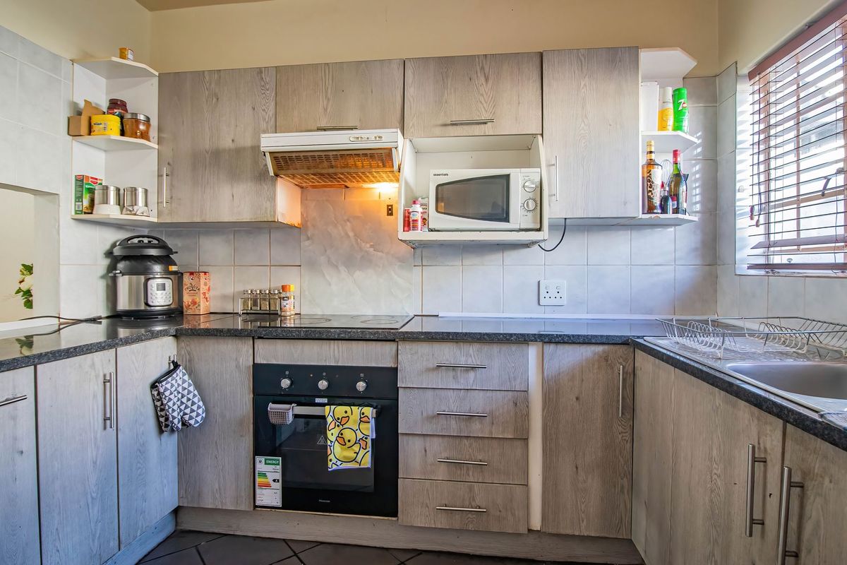 Functional kitchen featuring wood-look laminate cabinetry, granite countertops, built-in oven, hob, and extractor fan with a tiled backsplash and natural light.