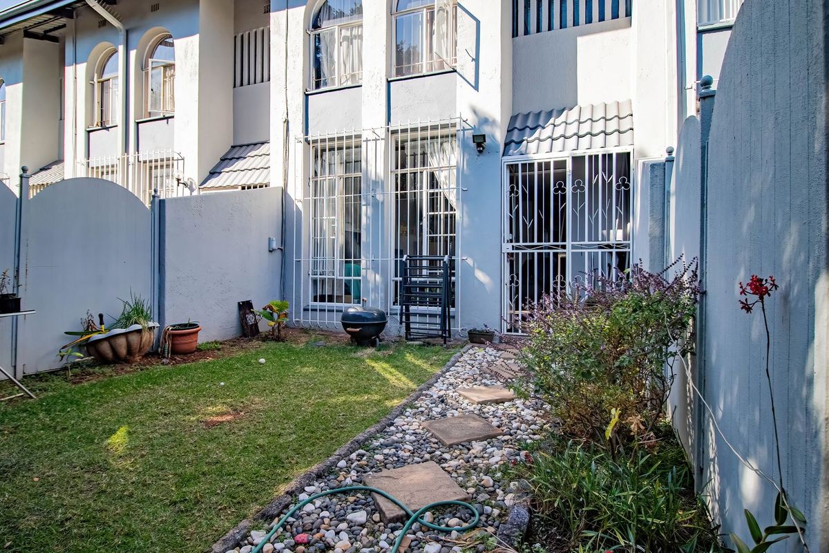 Rear view of the townhouse featuring a small private garden, paved pathway, and secure access points with security gates and bars.