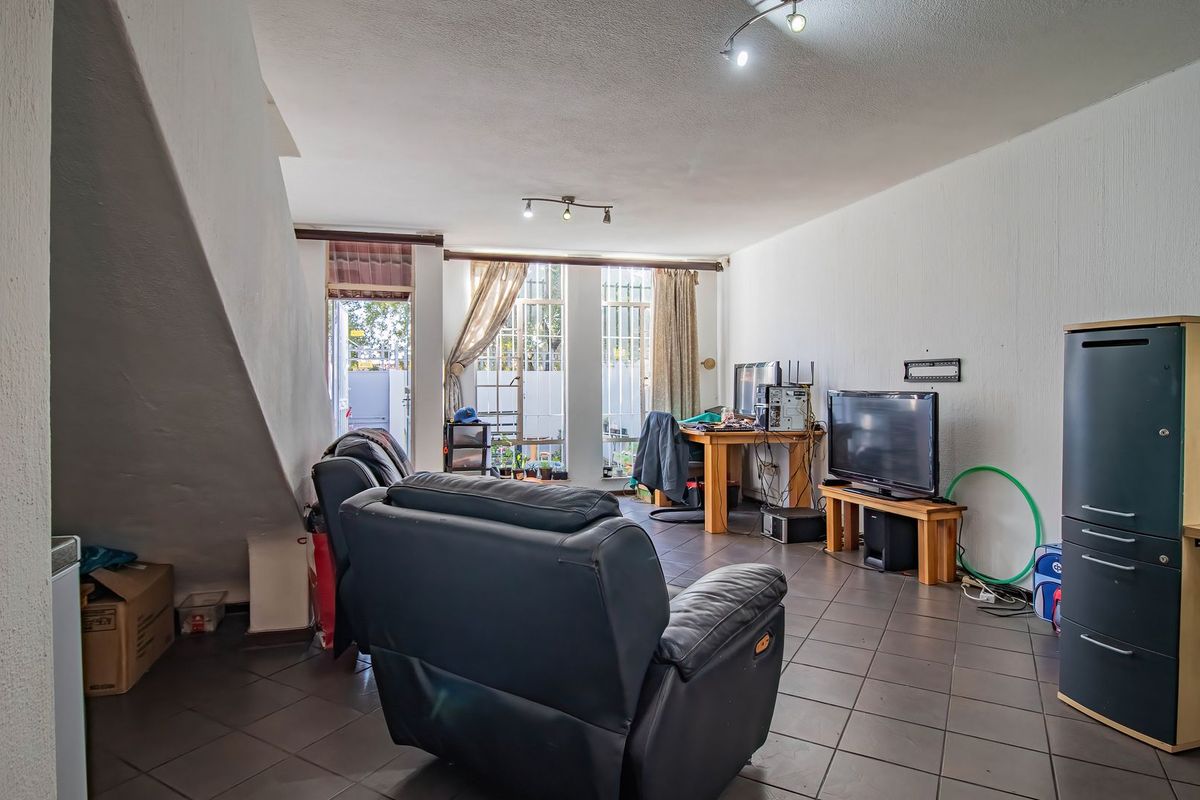 A spacious living room featuring tiled flooring, track lighting, and direct access to an outdoor area through a security gate.