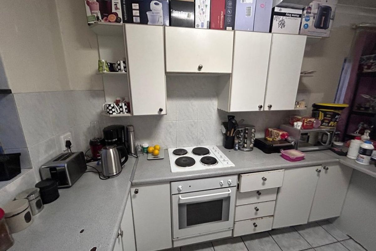 A functional kitchen featuring white cabinetry, a built-in oven, electric hob, and tiled splashback, offering a practical layout for daily meal preparation.