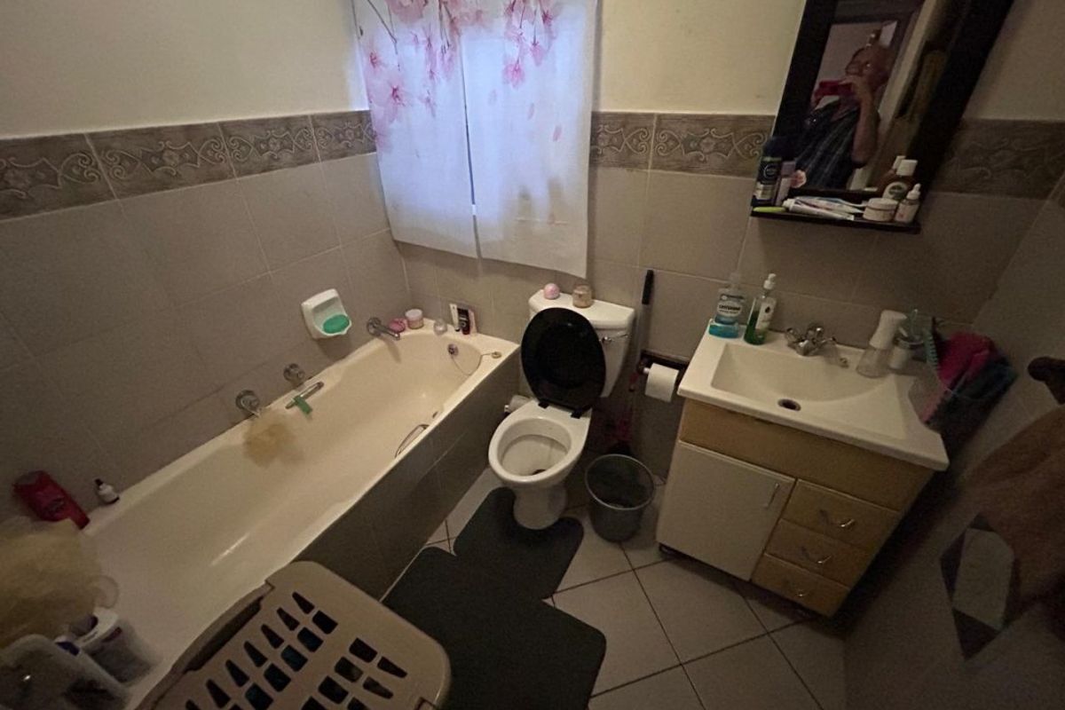 A functional bathroom featuring a bathtub, toilet, and vanity cabinet with a washbasin, finished with neutral wall and floor tiling.
