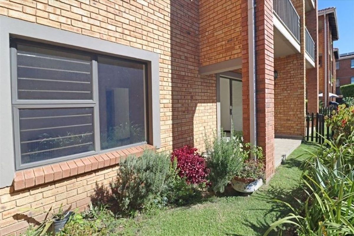 Rear exterior view of a townhouse featuring a face brick facade, aluminium window frames with security bars, and a covered patio area.