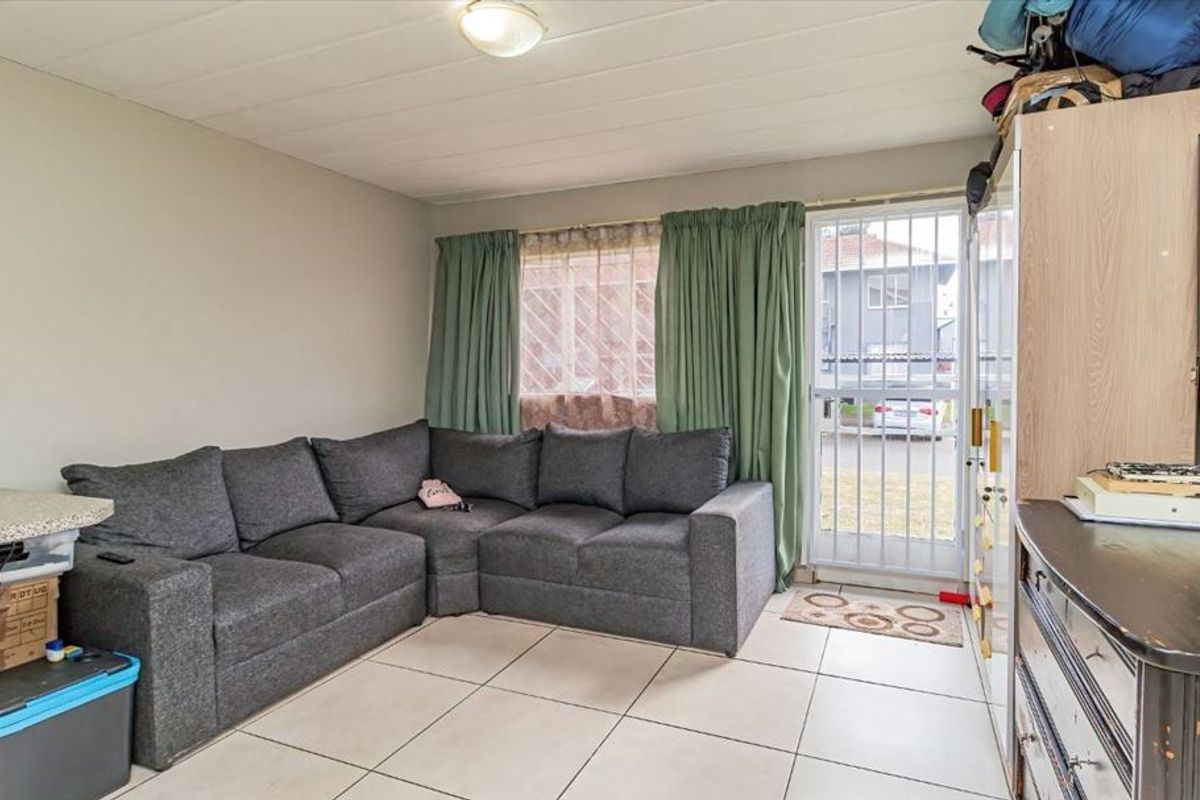 A functional living room featuring tiled flooring, a security gate leading to the exterior, and neutral wall finishes.
