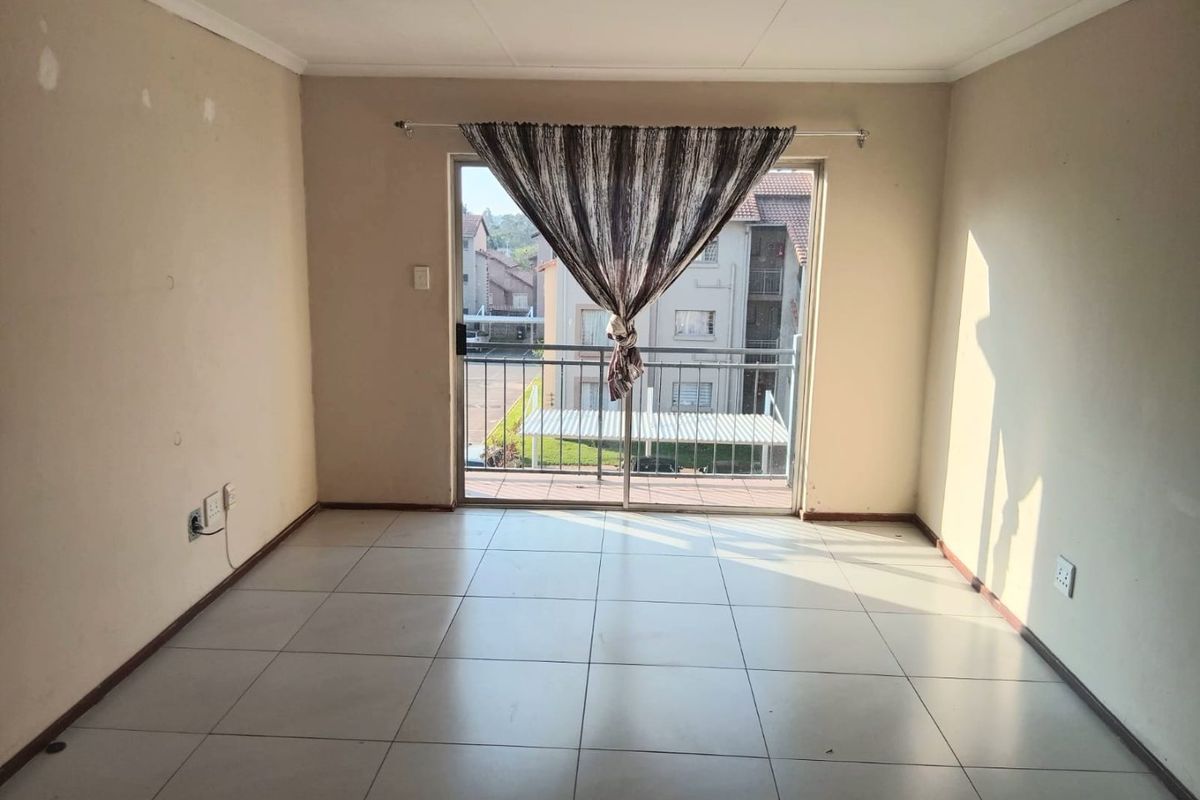 An empty living room featuring tiled flooring and a sliding glass door providing access to a balcony.