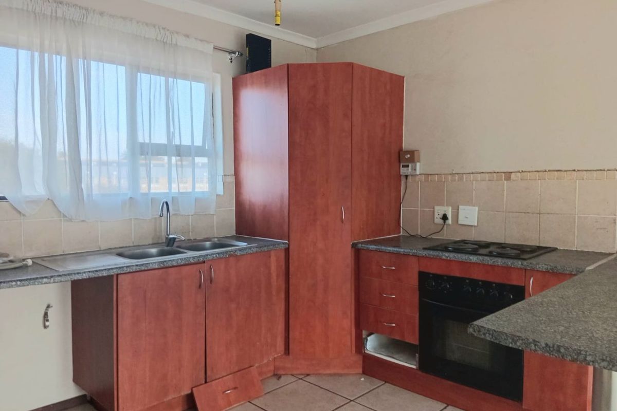 A functional kitchen featuring laminate cabinetry, a built-in oven and hob, double sink, and tiled backsplash, currently requiring minor repairs and cosmetic updates.