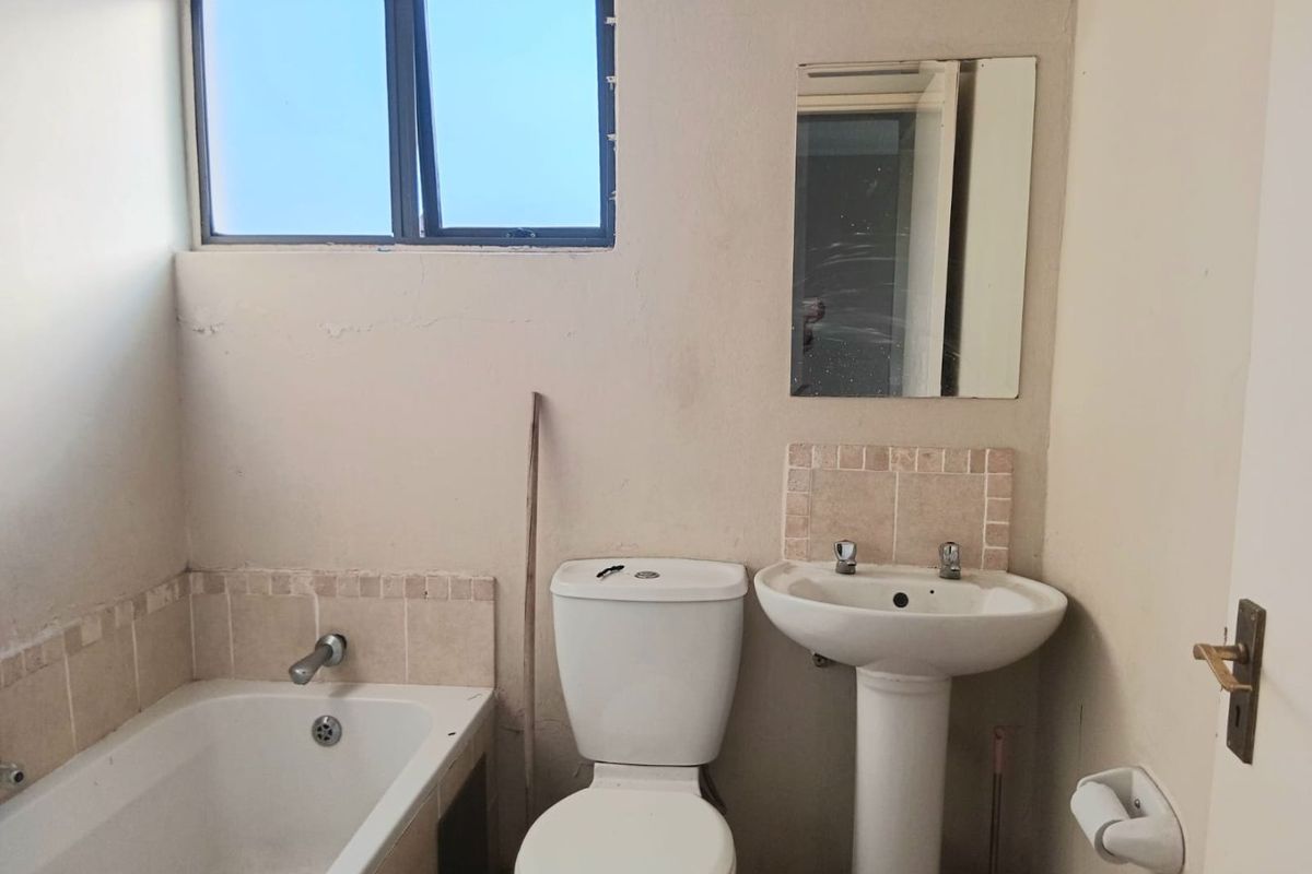 A functional bathroom featuring a standard bathtub, pedestal basin, and toilet, requiring cosmetic updates to the wall finishes.