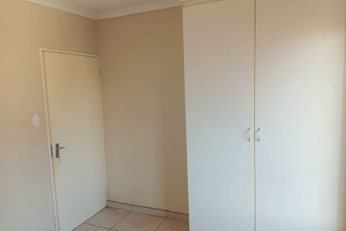 A clean, empty bedroom featuring neutral wall tones, tiled flooring, and a functional built-in wardrobe.