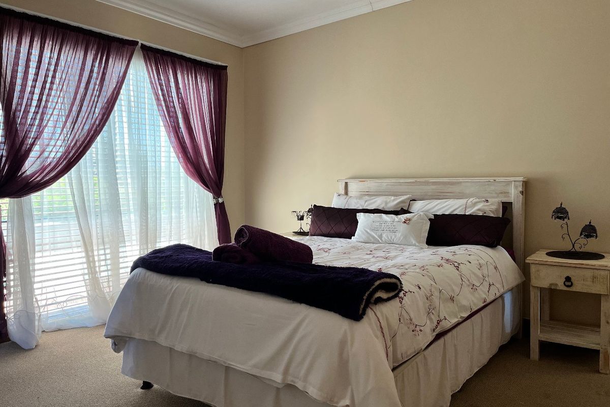 A comfortable bedroom featuring neutral wall tones, carpeted flooring, and a sliding glass door providing natural light and access to the exterior.