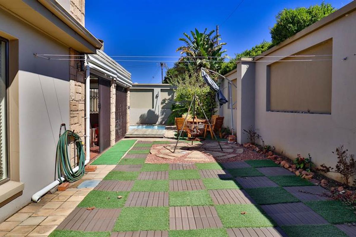 A private rear courtyard featuring a small swimming pool, paved and artificial turf sections, and high boundary walls for added privacy.