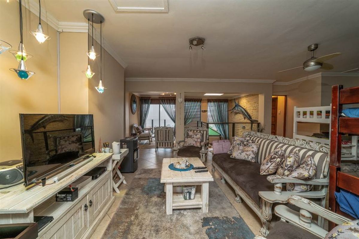 A spacious living room featuring tiled flooring, a ceiling fan, and an exposed brick feature wall, with direct access to an outdoor area.