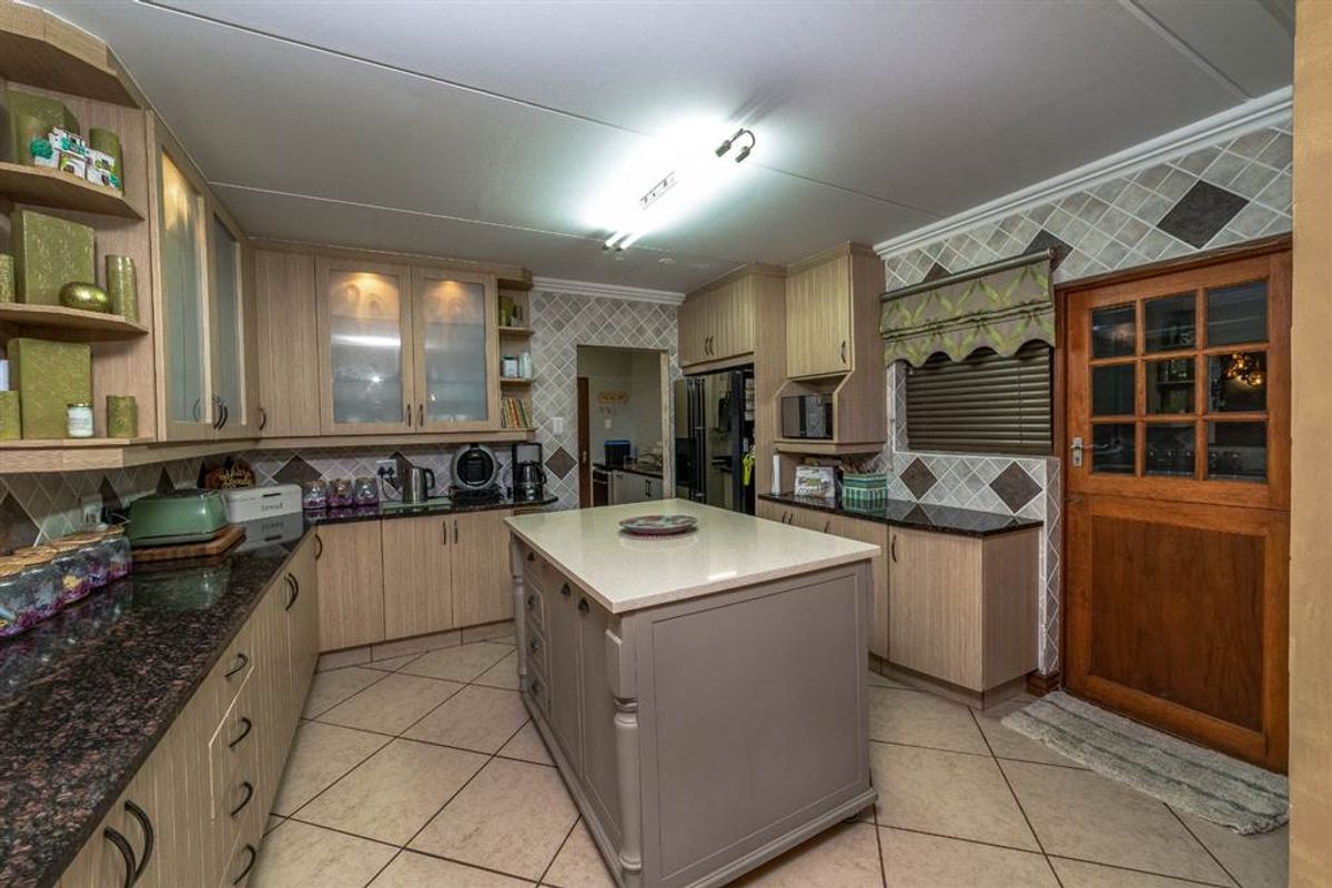 A functional kitchen featuring a central island, granite countertops, ample built-in cabinetry, and tiled flooring with a classic timber door.