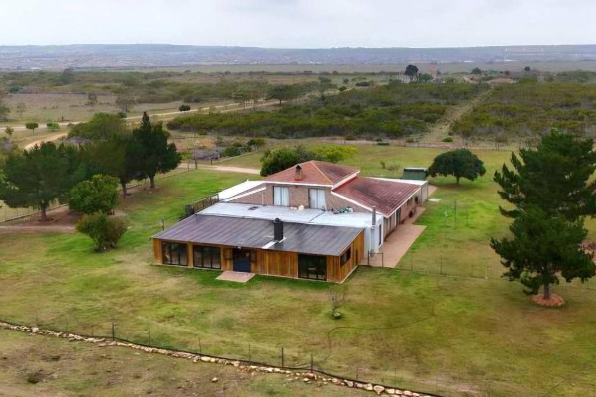 Aerial view of a farm property featuring a multi-section dwelling with a combination of tiled and metal roofing, set within a large rural landscape.