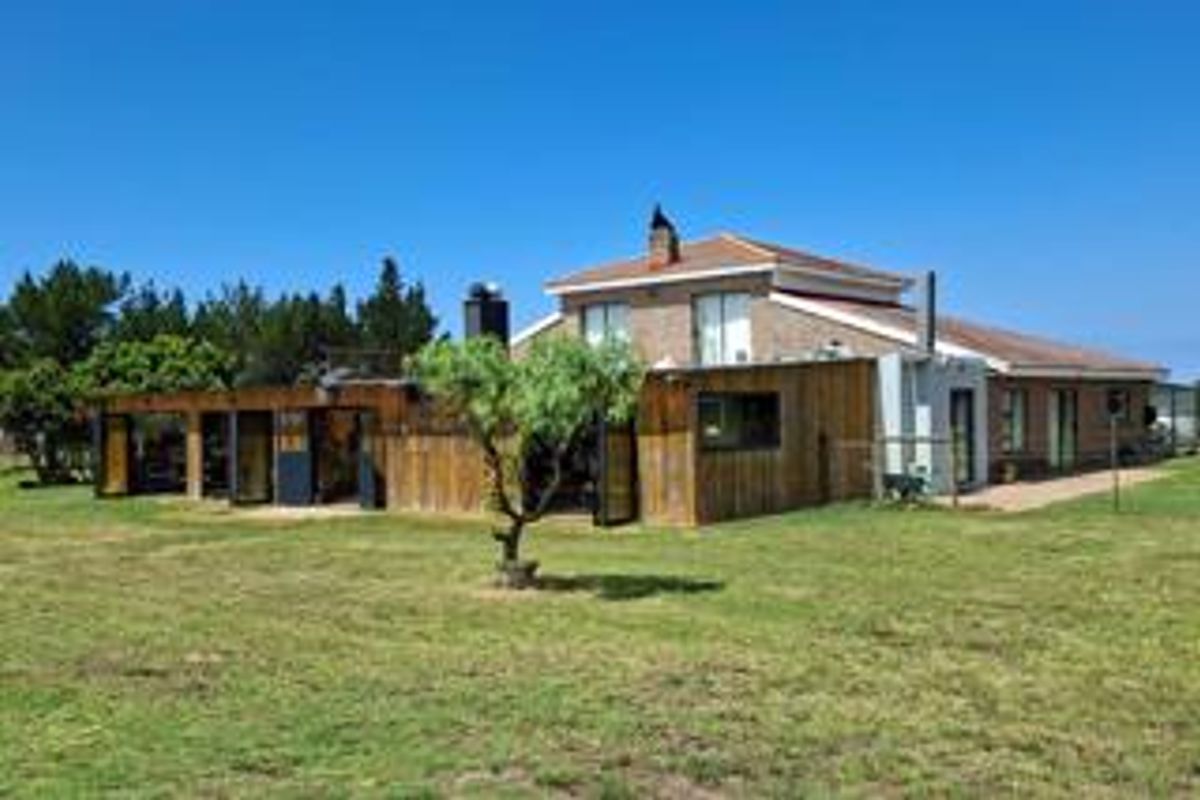 Rear view of the farm property featuring a combination of brick and timber cladding, a covered patio area, and a spacious lawn.
