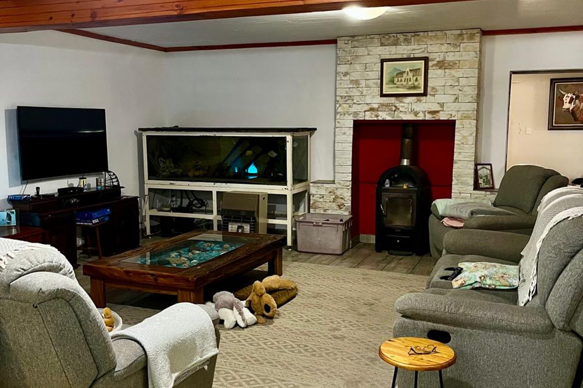 A cozy living room featuring a wood-burning stove with a stone fireplace surround, exposed timber ceiling beams, and durable tiled flooring.
