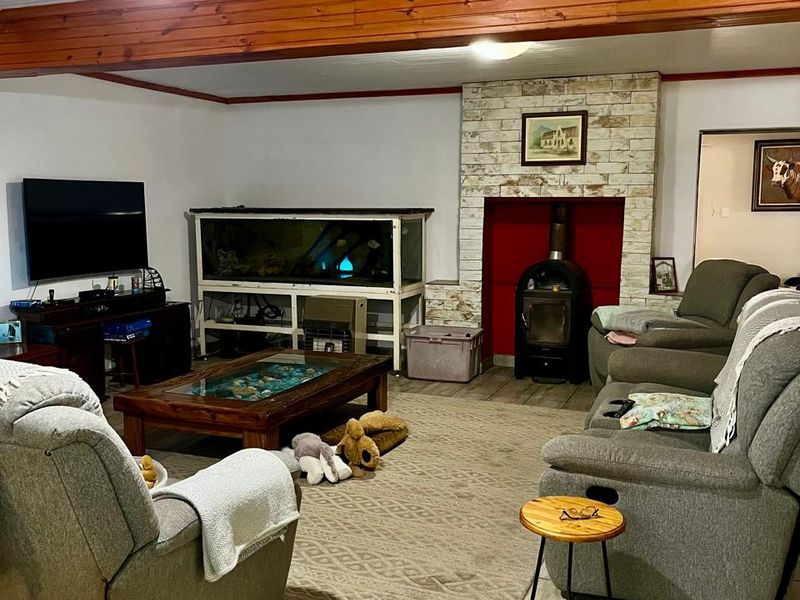 A cozy living room featuring a wood-burning stove with a stone fireplace surround, exposed timber ceiling beams, and durable tiled flooring.