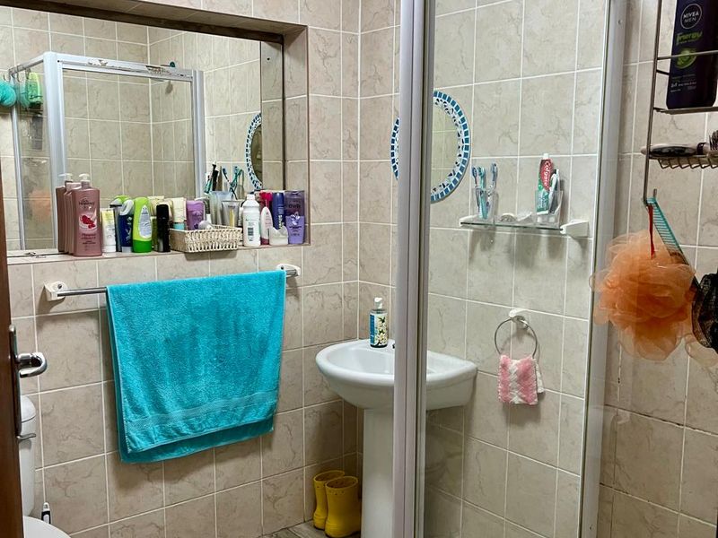 A functional bathroom featuring a pedestal basin, a shower enclosure, and neutral wall and floor tiling.