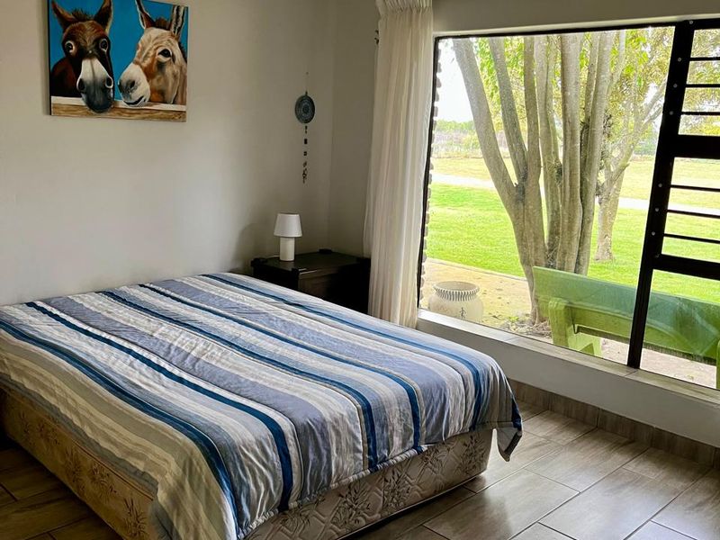 A bright bedroom featuring large windows with garden views and durable tiled flooring, offering a comfortable and well-maintained living space.