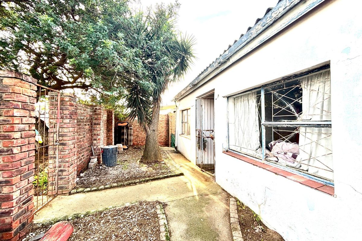 Rear exterior view of the property showing a concrete pathway, brick boundary wall, and visible wear to the building facade and window frames.