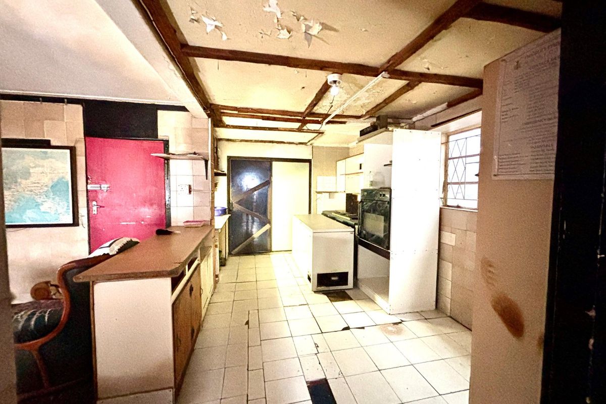 A dated kitchen featuring tiled flooring, built-in oven, and breakfast counter, currently requiring significant ceiling and surface repairs to restore functionality.
