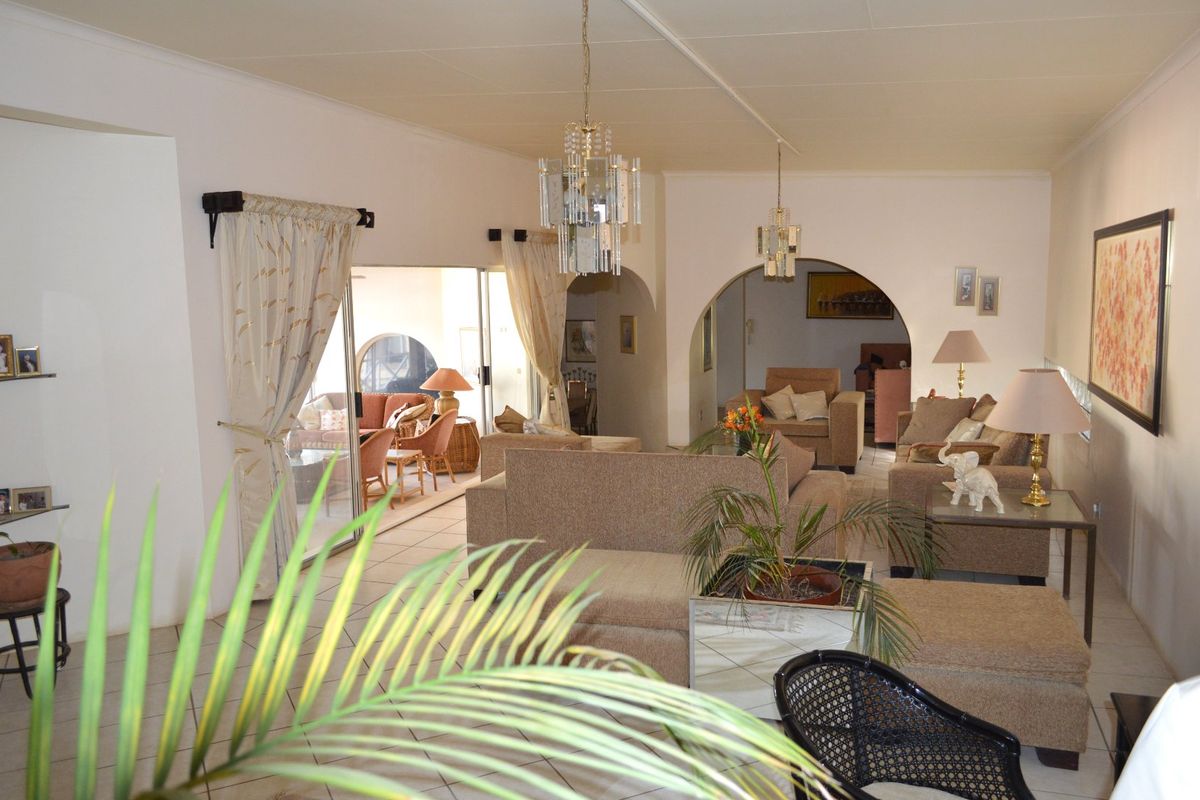 Spacious living area featuring tiled flooring, elegant archways, and classic crystal chandeliers, with direct access to an adjoining patio through sliding glass doors.