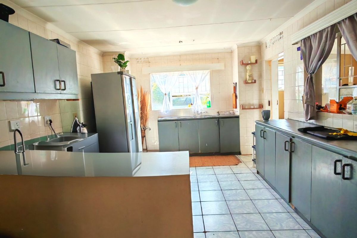 A functional kitchen featuring extensive built-in cabinetry, tiled surfaces, and a double sink, offering a practical layout with potential for modern cosmetic updates.
