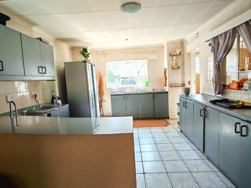 A functional kitchen featuring extensive built-in cabinetry, tiled surfaces, and a double sink, offering a practical layout with potential for modern cosmetic updates.