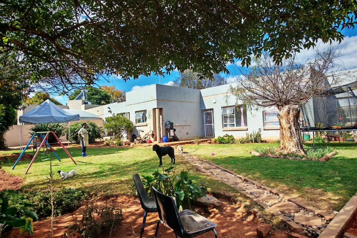 A view of the rear garden featuring a stone pathway, established lawn, and mature trees leading to the back facade of the house.