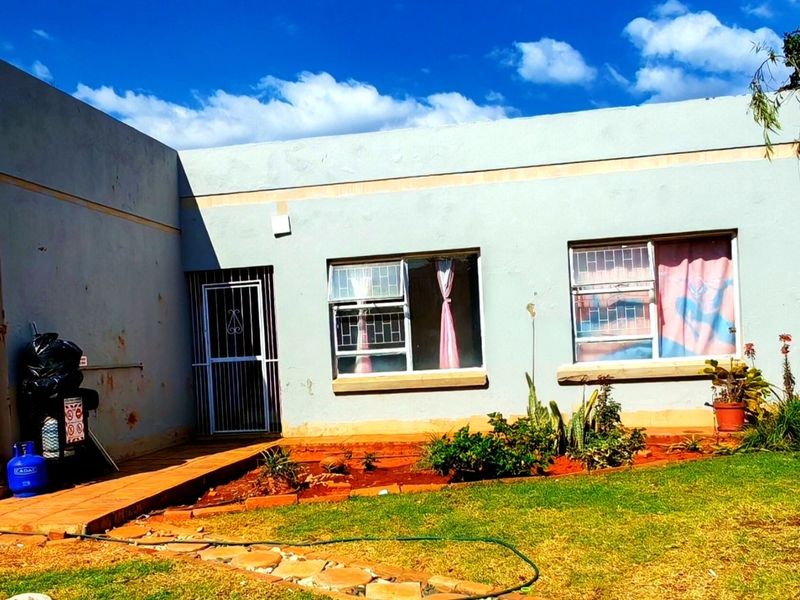 Rear view of a single-story house featuring a concrete patio, security gates, and established garden area with visible exterior wall maintenance required.