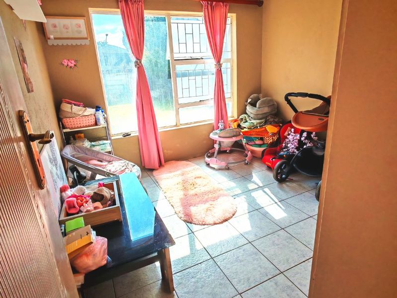 A bedroom featuring tiled flooring and large windows with security bars, providing natural light.
