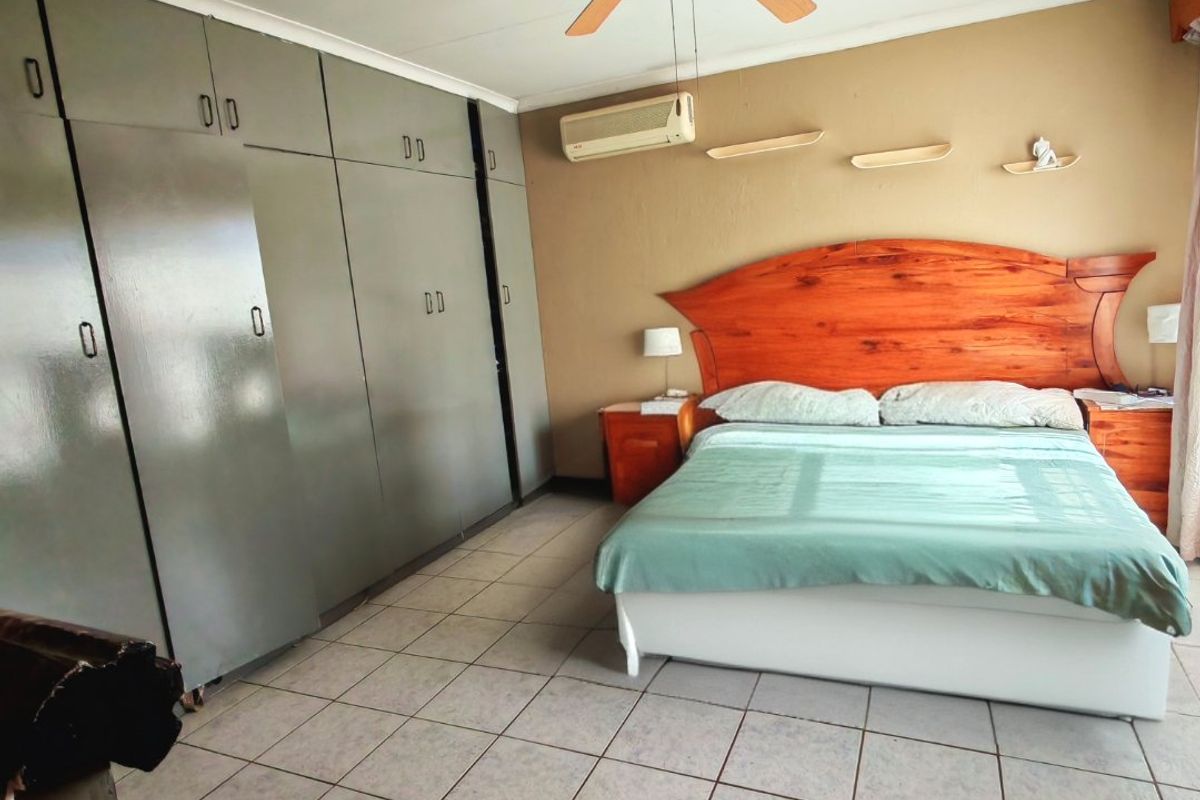Spacious bedroom featuring extensive built-in cupboards, a ceiling fan, and a wall-mounted air conditioning unit with neutral tiled flooring.