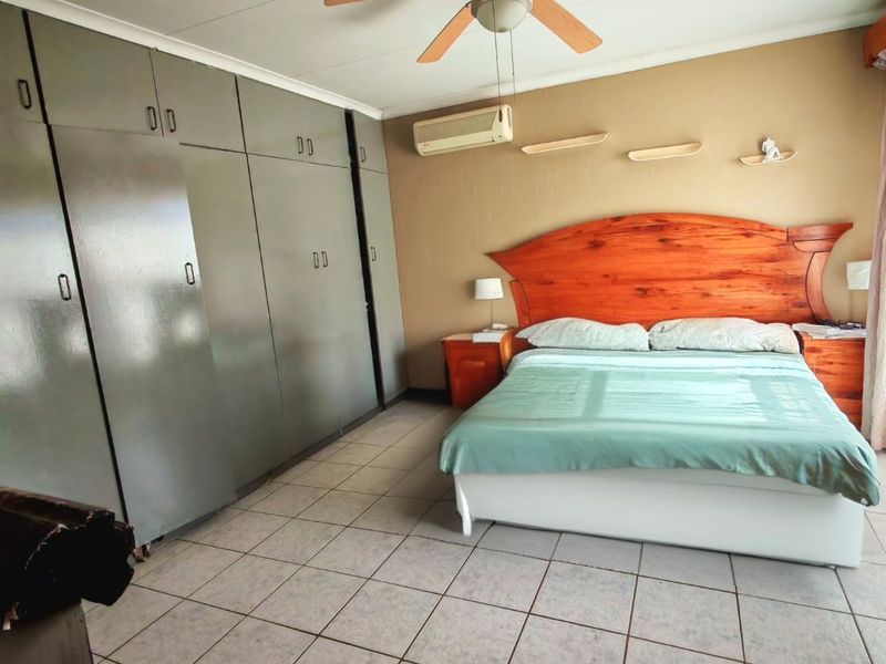 Spacious bedroom featuring extensive built-in cupboards, a ceiling fan, and a wall-mounted air conditioning unit with neutral tiled flooring.