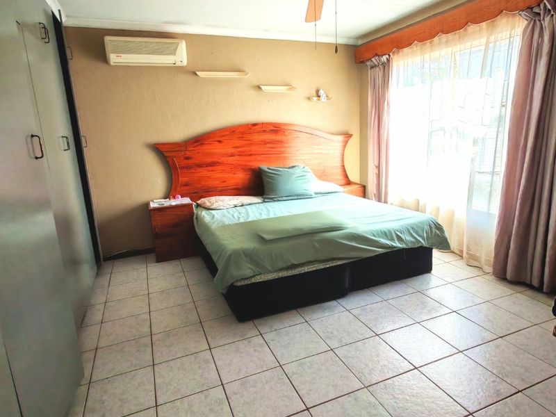 A bedroom featuring tiled flooring, a ceiling fan, a wall-mounted air conditioning unit, and built-in storage cupboards.