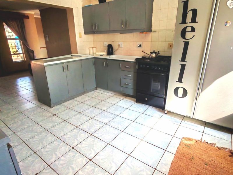 A functional kitchen featuring fitted cabinetry, tiled flooring, a tiled backsplash, and a freestanding stove, offering potential for modern updates.